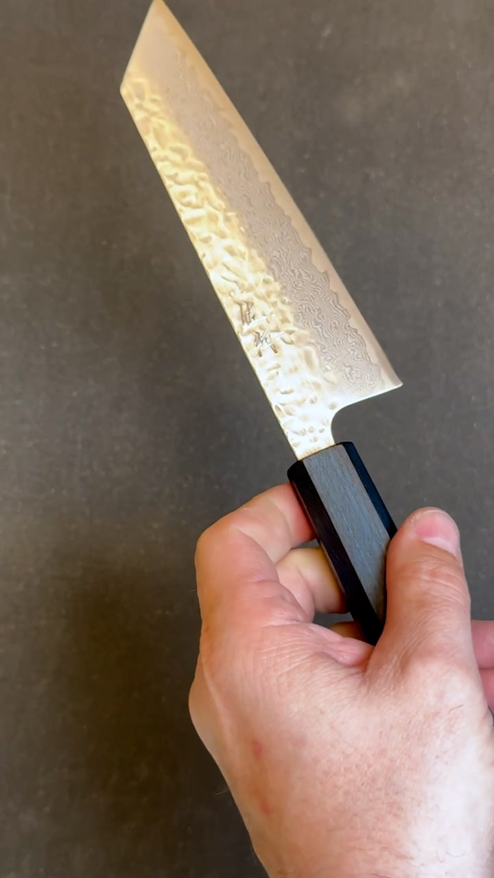 Hand holding a bunka knife with a textured blade against a dark background