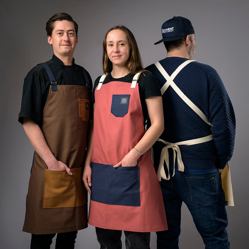 Three people wearing different aprons against a gray background