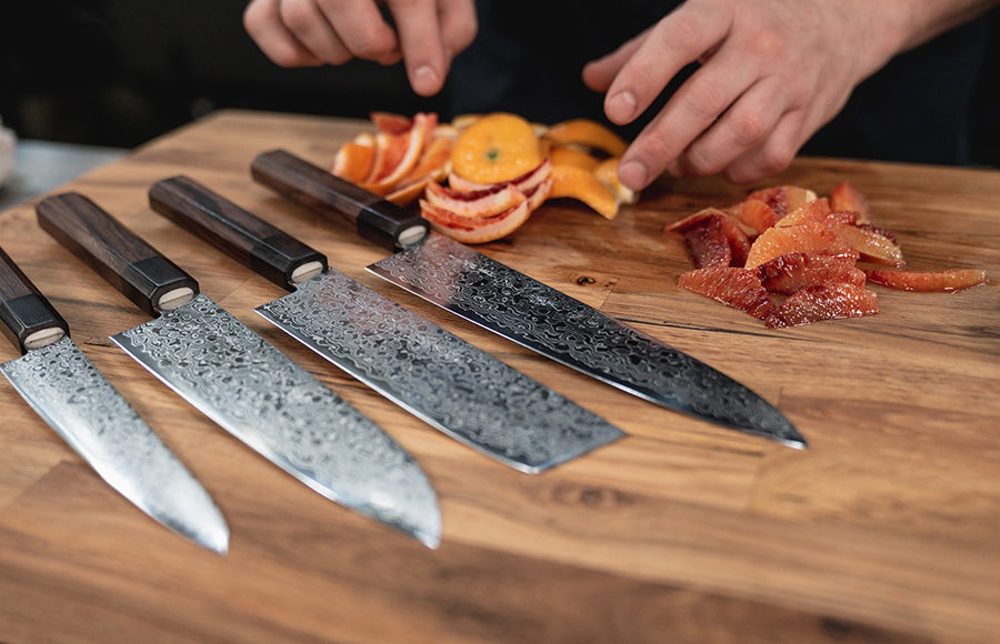 Set of Damascus steel knives on a wooden cutting board with sliced fruit.