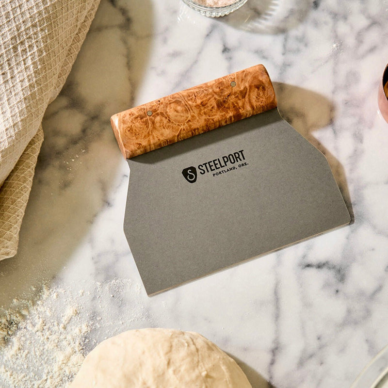 Cutting Board Scraper with wooden handle on a marble surface
